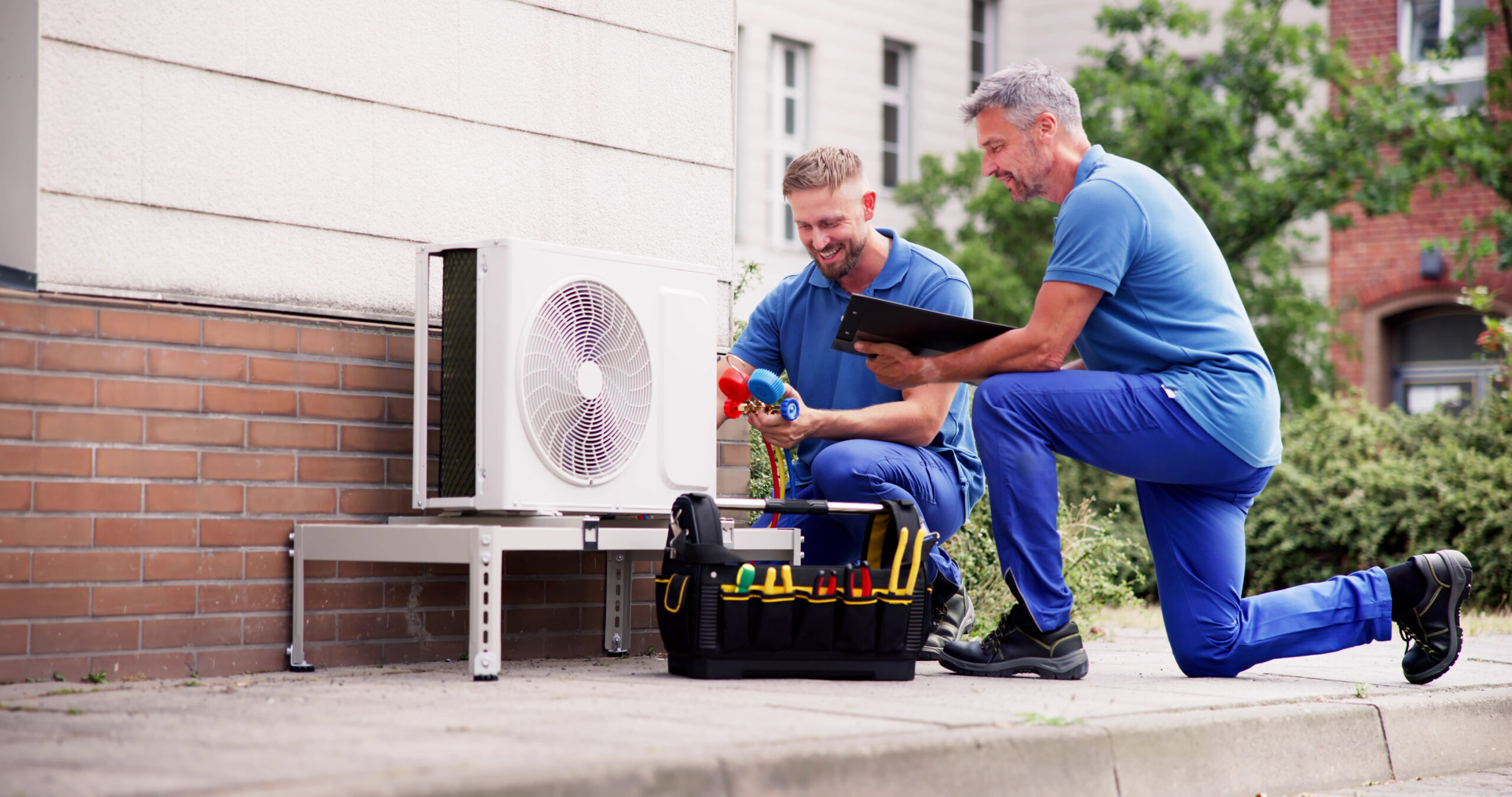 Two men working on a air conditioner outside.