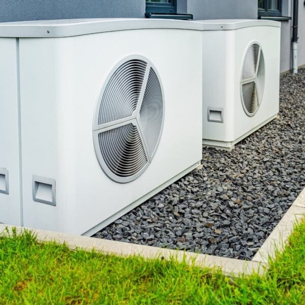 Two air conditioners are sitting outside on the ground.