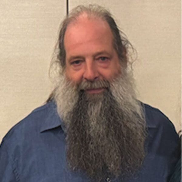 A man with long hair and beard wearing a blue shirt.